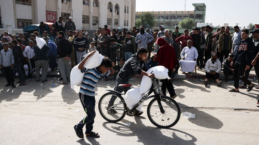 A child carries a bag of humanitarian aid on his back as another uses a bicycle, in Rafah in the southern Gaza Strip on November 26, 2023.