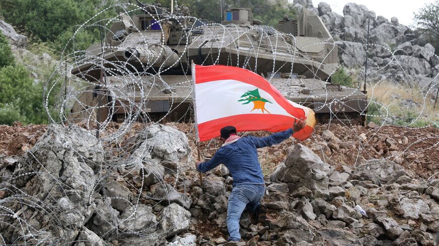 A protester plants a flag bearing a Lebanese cedar across the fence from an Israeli tank at the Blue Line near the southern Lebanese village of Kfar Shuba, in the Israel-Lebanon border region, June 9, 2023.