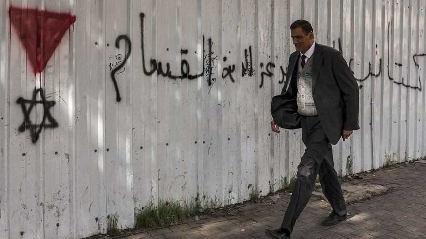 A Palestinian man walks past a graffiti on a wall showing the Star of David under an inverted "red triangle", a symbol used by the Palestinian Hamas movement's military wing al-Qassam Brigades to identify Israeli targets in their videos, in the city of Hebron in the occupied West Bank on December 16,2023. (Photo by HAZEM BADER / AFP) (Photo by HAZEM BADER/AFP via Getty Images)