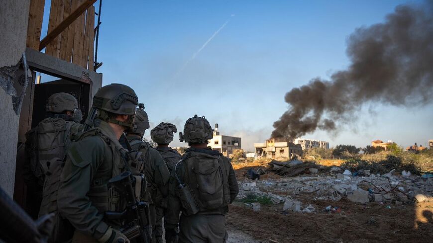 Israeli soldiers watch as smoke billows from a building in Gaza