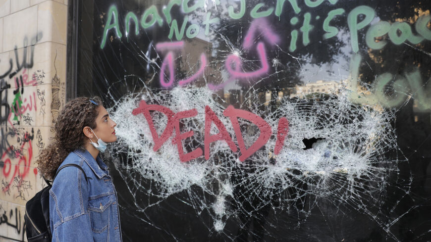 A Lebanese woman looks at graffiti on a smashed glass facade in the heart of the capital Beirut on October 25, 2019 as anti-corruption demonstrators cut off major roads across the country for a ninth day, pledging to carry on with their protests despite the president offering to meet their representatives. - The entire political class has been targeted in days of unprecedented street demos that have dominated city centres and closed banks, schools and universities across Lebanon. (Photo by ANWAR AMRO / AFP)