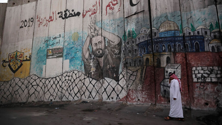 A Palestinian man walks alongside Israel's separation barrier painted with an image of jailed Fatah leader Marwan Barghouti, in the West Bank town of al-Azariya, on the outskirts of Jerusalem, Nov. 8, 2021.