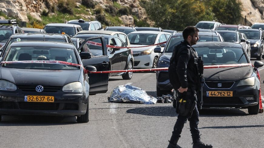 A member of the Israeli security forces walks near a body lying on the road amid vehicles at the scene of a shooting attack on February 22, 2024, near Maale Adumim settlement, east of Jerusalem