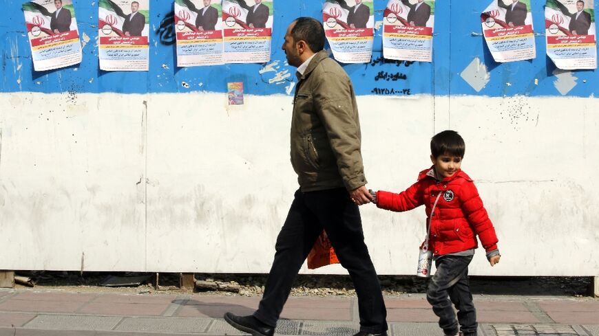 A man and a child walk past electoral campaign posters bearing portraits of a parliamentary candidate during the first day of election campaigning in Tehran
