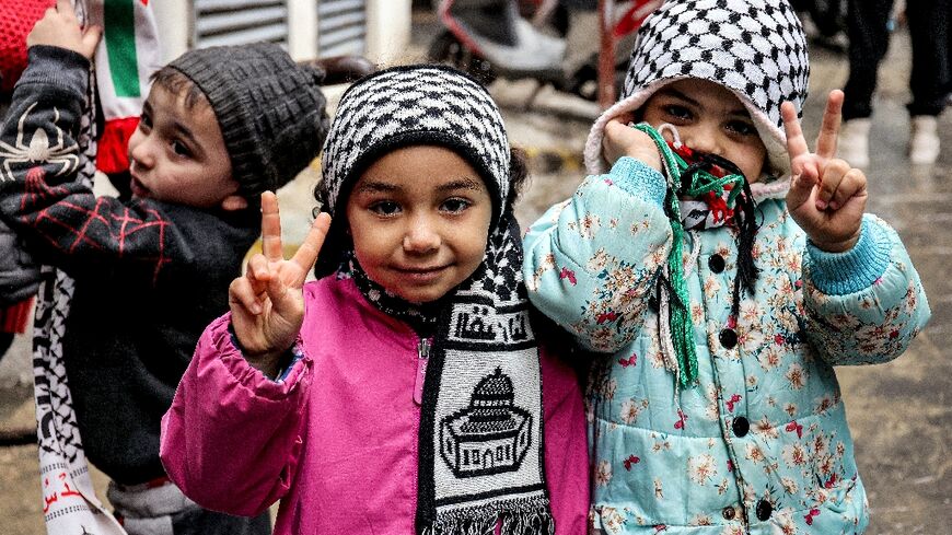 Children wearing Palestinian keffiyeh scarves gesture as they stand along an alley in the Burj al-Barajneh camp for Palestinian refugees in southern Beirut