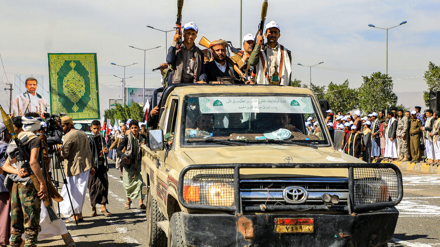 Men armed with rocket-propelled grenade (RPG) launchers and assault rifles ride in the back of a pickup vehicle parading before a large banner depicting the Koran, Islam's Holy Book, and Hussein Badreddin al-Houthi, the slain leader of Yemen's Houthi movement who was killed in 2004, during a pro-Palestinian rally in the Houthi-held capital Sanaa on Feb. 7, 2024.