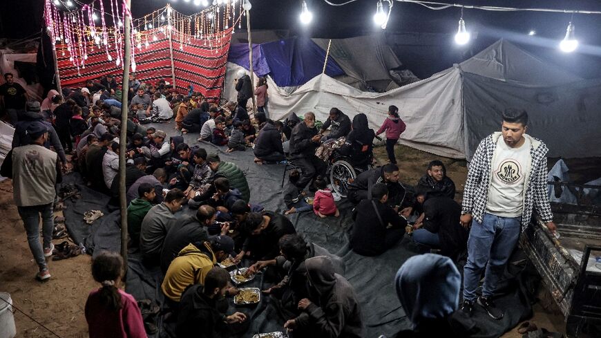 At a camp for the displaced in Rafah, the southern Gaza Strip, Palestinians share an iftar meal to break their fast on the first day of Ramadan