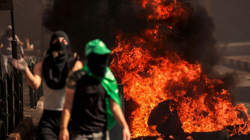 Masked Palestinian protesters walk near flaming tires during clashes with Israeli forces following a rally in solidarity with Gaza by supporters of the Fatah and Hamas movements, in the city of Hebron in the occupied West Bank on October 13, 2023. AFP correspondents and a security official reported clashes after rallies in solidarity with war-battered Gaza in Ramallah, Nablus, Tulkarm, Hebron and other cities and towns, with the Palestinian Red Crescent reporting dozens wounded across the West Bank, some cr
