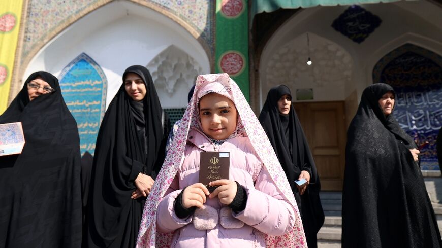 An Iranian child shows the document of a family member as women queue in front of a polling station to cast their ballots in Tehran