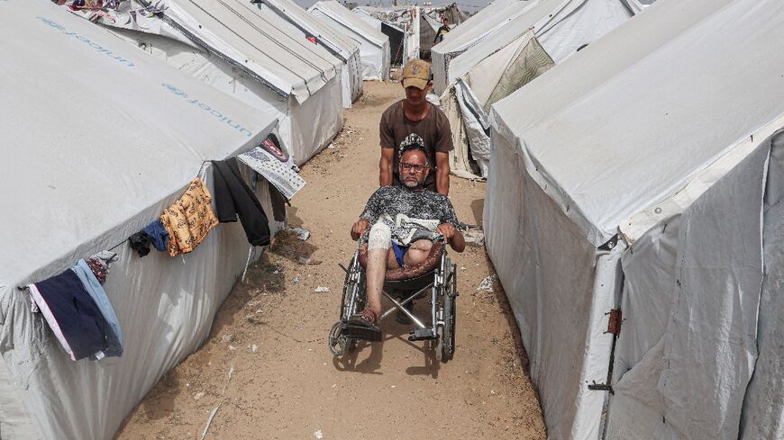 Injured Palestinian Tamer Abu Ali, 47, whose leg was amputated during the Israel-Hamas war, is pushed by his son in a camp for displaced people in Rafah