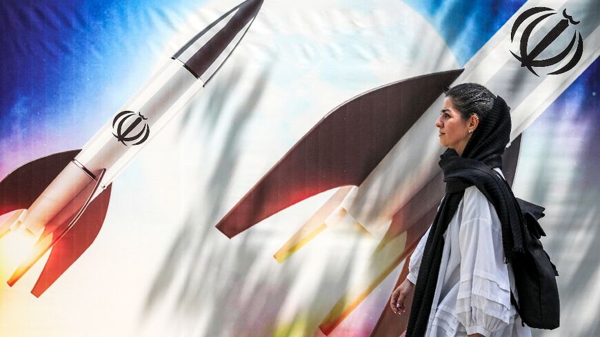 A woman walks past a banner depicting missiles bearing the emblem of the Islamic Republic of Iran in central Tehran