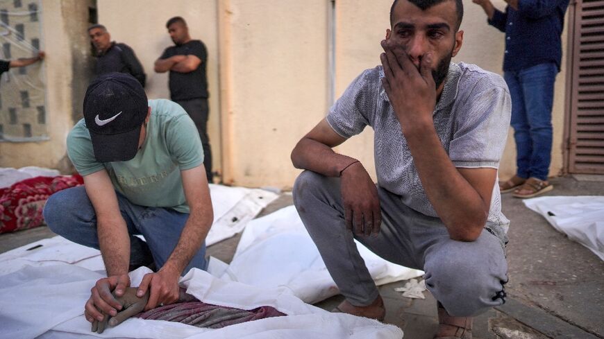 In the yard of Al-Aqsa Martyrs Hospital in Deir al-Balah, central Gaza, a Palestinian man reacts as another holds the hand of a person killed in Israeli bombardment