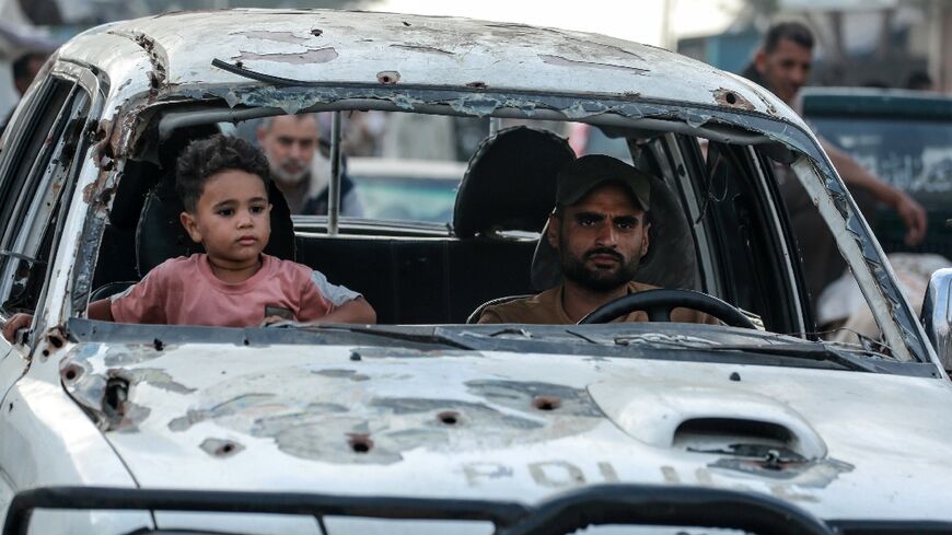 A Palestinian child sits next to a man driving a damaged car in Deir el-Blaha in the central Gazas Strip