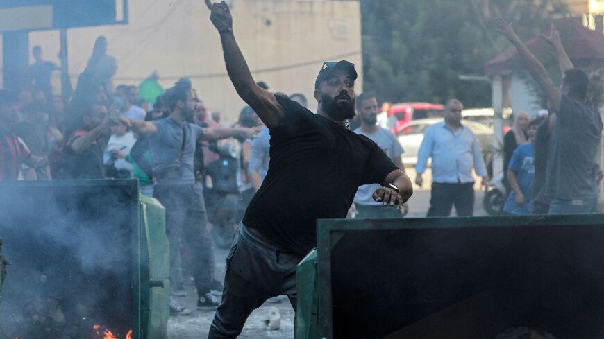 A man throws a stone from behind a burning rubbish container as displaced people who fled Israeli bombardment in Beirut's southern suburbs clash with Lebanese security forces in central Beirut