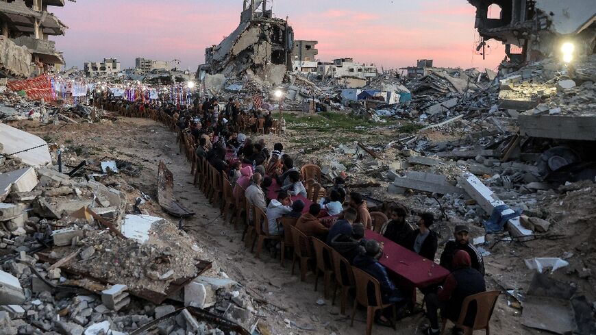 People gather among the rubble of destroyed buildings for a communal iftar fast-breaking meal on the second day of the Muslim holy month of Ramadan in in Gaza City's Tal al-Hawa district