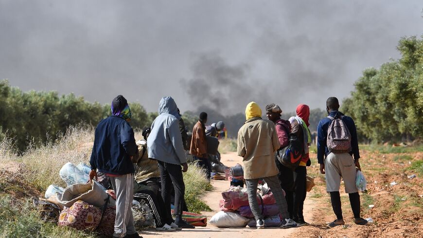 Migrants look on as smoke rises from what used to be their makeshift camp at El Amra