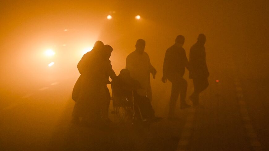 A wheelchair-user is helped across a road in dangerously low visibility in the southern Iraqi city of Basra on Monday.