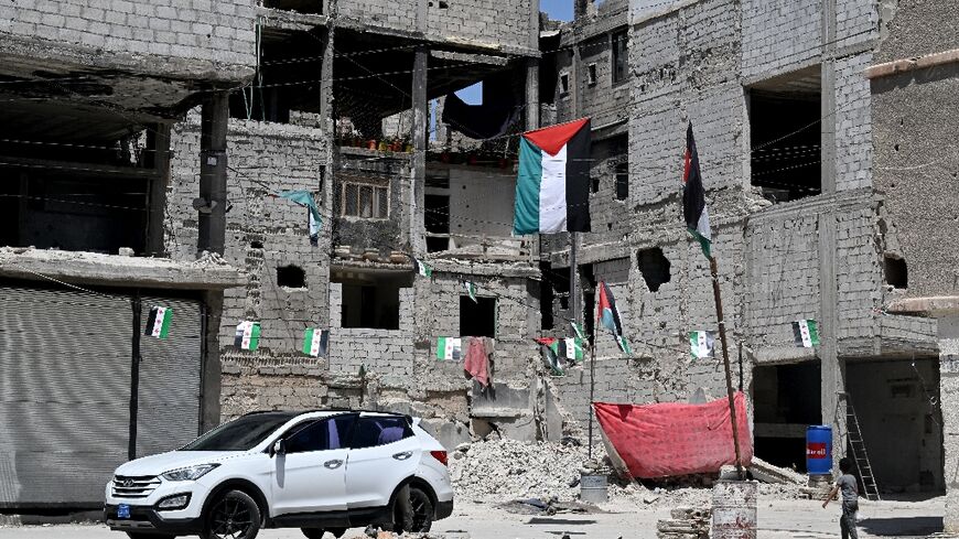 A boy walks under Palestinian and Syrian flags hanging outside buildings damaged during Syria's 14-year civil war in the Yarmuk refugee camp in southern Damascus