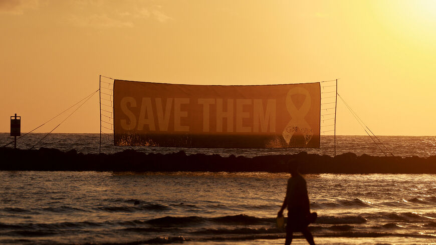 FILE PHOTO: A person walks on the beach, as a sign asks for the safe return of hostages held in Gaza since October 7, 2023 attack on Israel by Hamas, near the U.S. Consulate in Tel Aviv, Israel, July 7, 2025. REUTERS/Ammar Awad/File Photo