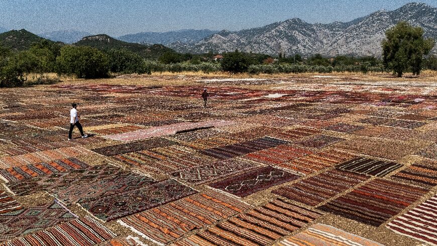Tourists walk on handwoven carpet laid out in an open field to soften their colours under sizzling sun in coastal city Antalya's Dosemealti district