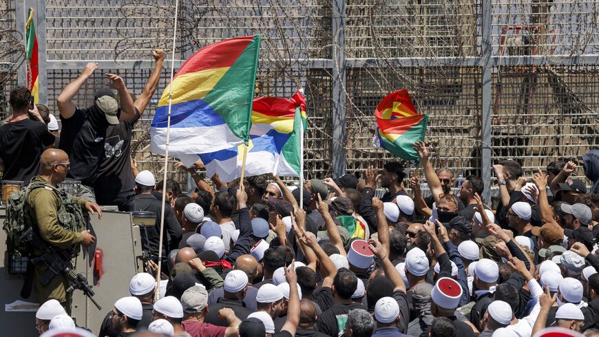 Members of the Druze community demonstrate before Israeli forces by the barbed-wire fence separating the Israeli-annexed Golan Heights and Syria near Majdal Shams, on July 16, 2025. 