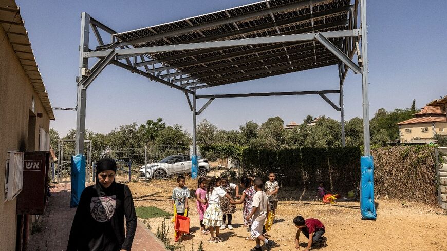 Children play beneath a scaffolding holding photovoltaic solar panels in the yard of a kindergarten in the Bedouin village of Umm Batin near Beersheva in Israel's southern Negev desert