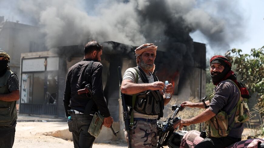 Bedouin fighters watch on impassively as a building goes up in smoke in the village of Al-Mazraa outside Sweida.