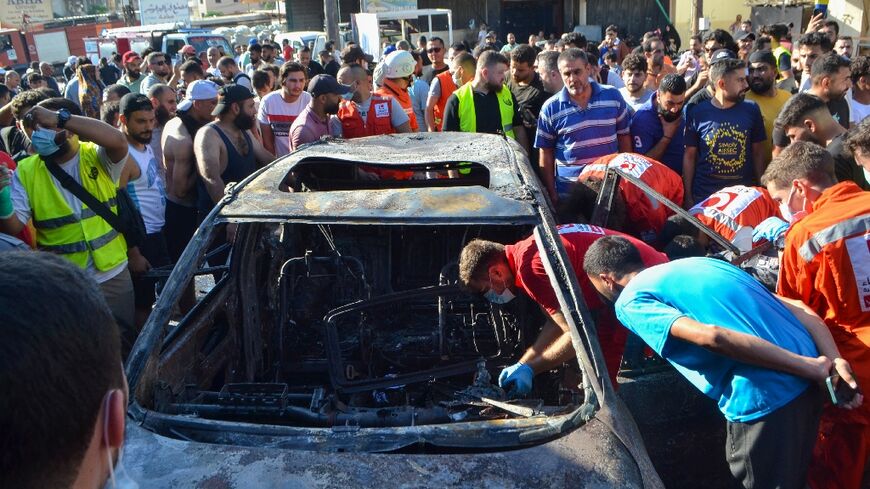 Onlookers gather around a burnt out car targeted in an Israeli strike near Lebanon's main northern city of Tripoli.
