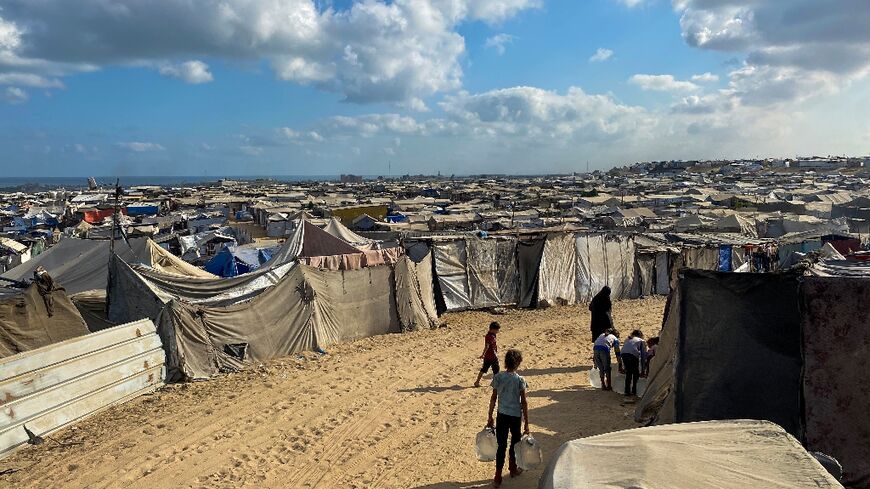 Palestinian children carry water past line after line of tents housing displaced families in the sand dunes of Mawasi on Gaza's Mediterranean coast.