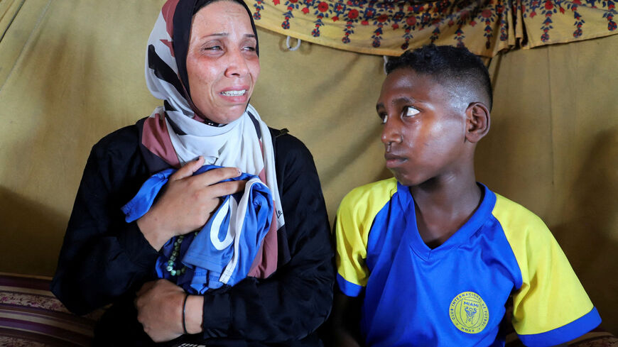 Doaa, the widow of late soccer player Suleiman Al-Obeid, known as the "Palestinian Pele," who was killed by an Israeli strike targeting people waiting for humanitarian aid, according to the Palestine Football Association, grieves while holding his shorts, as her son sits beside her inside their tent in Gaza City August 9, 2025. REUTERS/Ebrahim Hajjaj     TPX IMAGES OF THE DAY