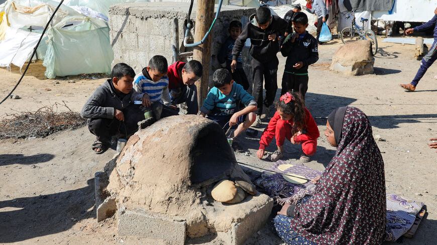 A Palestinian woman bakes bread as children sit next to her, while Gaza residents face crisis levels of hunger and soaring malnutrition, in Khan Younis in the southern Gaza Strip January 24, 2024. REUTERS/Arafat Barbakh/File Photo
