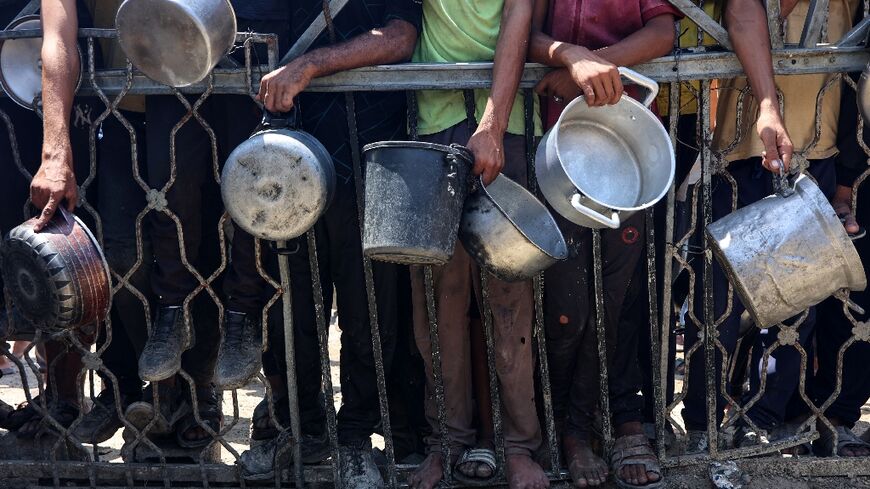 Palestinians carry empty pots as they wait to receive lentil soup at a food distribution point in Gaza City on August 2, 2025

