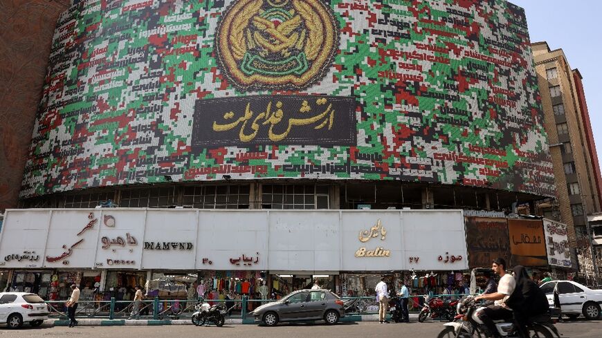 Iranians drive past a billboard with the colors of Iran's national flag
