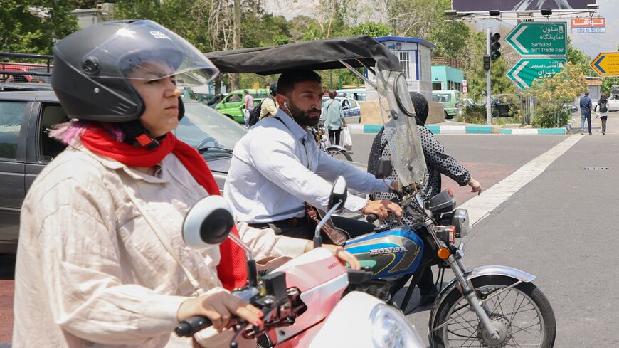 A man and a woman ride their motorcycles past a billboard in the background bearing a portrait of Iran's late President Ebrahim Raisi in central Tehran, on May 21, 2024.