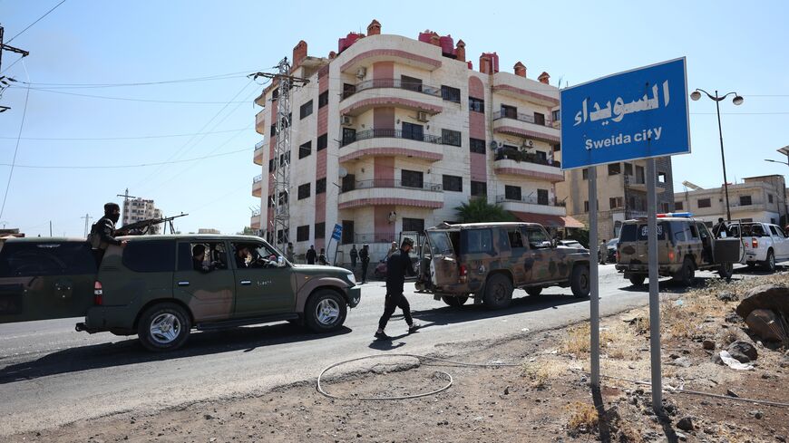 A convoy of Syrian military and security forces passes a sign for Sweida city on July 15, 2025, near Sweida, Syria. 