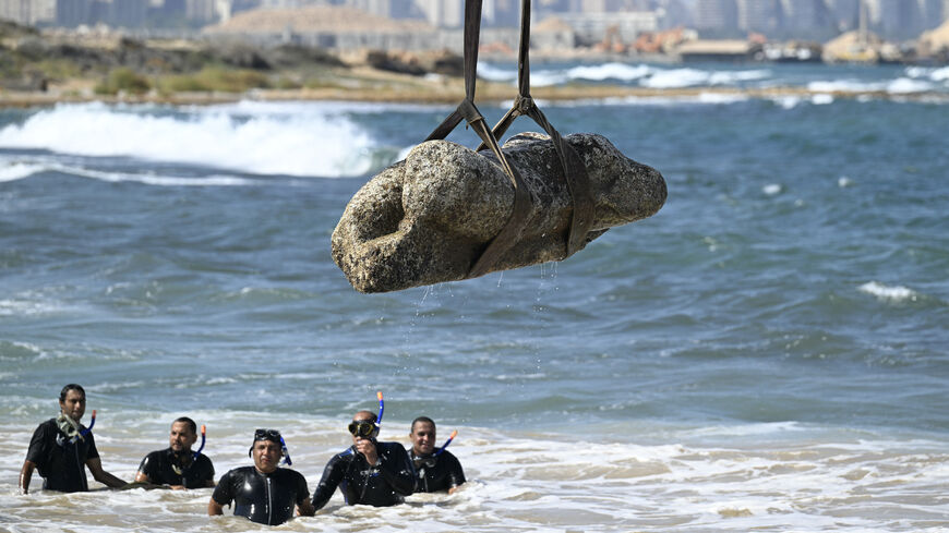 Divers watch as a crane pulls an artifact from the waters at Abu Qir bay in Alexandria on Aug. 21, 2025, as part of an event organized by the Ministry of Tourism and Antiquities to recover sunken antiquities. 