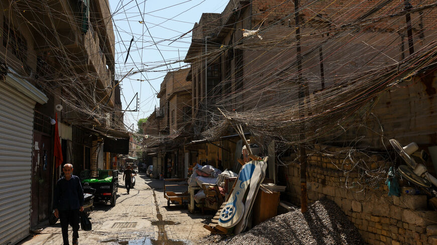 People walk along an old street as a tangled web of electrical wires from a generator supplying homes with electricity hangs above buildings, in Baghdad, Iraq, September 10, 2025. REUTERS/Thaier Al-Sudani
