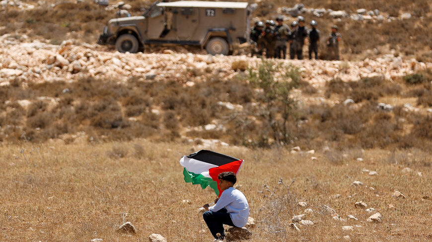 A boy holds a Palestinian flag during a demonstration against what Palestinians say is Israel's confiscation of their land, as Isareli security forces stand guard, in Raba, near Jenin, in the Israeli-occupied West Bank July 18, 2025. REUTERS/Raneen Sawafta/File Photo