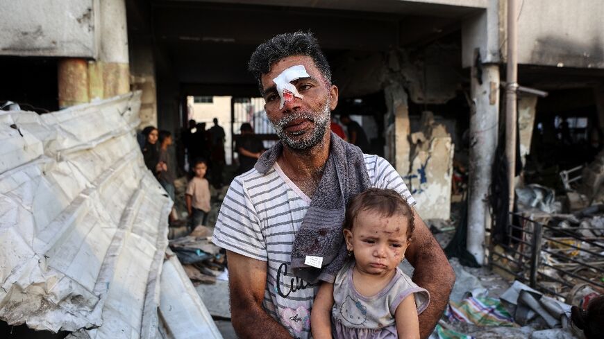 An injured man carries a toddler after a school in Gaza City being used to shelter displaced Palestinians was hit by an Israeli strike