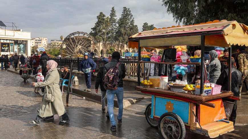 People and street vendors move past one of Hama's landmark historic water wheels on a bridge over the Orontes riverbank in the heart of the central Syrian city on Dec. 30, 2024. 