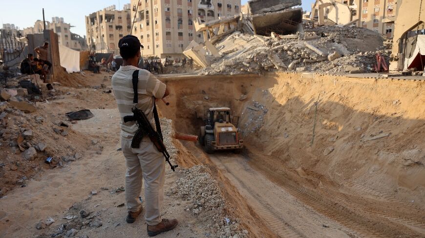 An armed Palestinian man looks at an excavator reportedly digging for the bodies of Israeli hostages