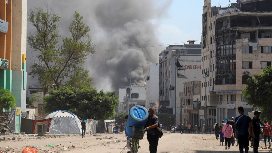 A Palestinian man pushes his bike with a tank as smoke rises from Israeli strikes, amid an Israeli military operation, in Gaza City September 22, 2025. REUTERS/Ebrahim Hajjaj