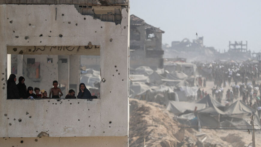 Women and children look out from a damaged building as Palestinians carry aid supplies that entered Gaza through Israel, in Beit Lahia, northern Gaza Strip, August 2, 2025. REUTERS/Mahmoud Issa