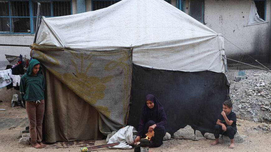A Palestinian woman builds a fire as children look towards it while beside a tent, after U.S. President Donald Trump announced that Israel and Hamas agreed on the first phase of a Gaza ceasefire, in Khan Younis in the southern Gaza Strip October 9, 2025. REUTERS/Ramadan Abed