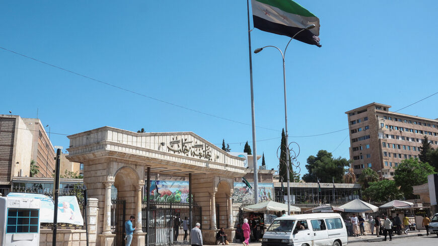 People walk near the Syrian flag, as U.S. President Donald Trump announced that he would order the lifting of sanctions on Syria, in Aleppo, Syria May 14, 2025. REUTERS/Mahmoud Hassano