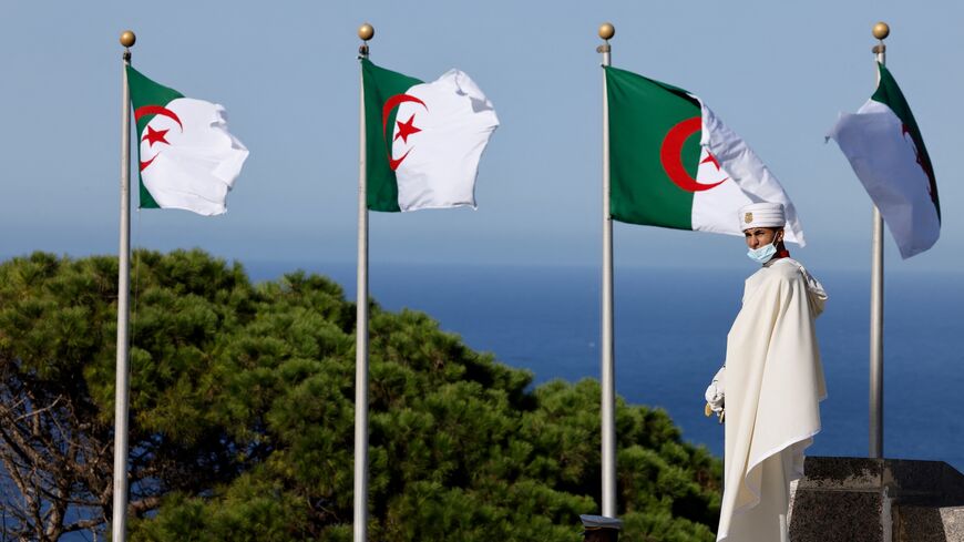 A man wearing a traditional cloth walks past national flags of Algeria near the Bay of Algiers in Algiers, on Aug. 25, 2022.