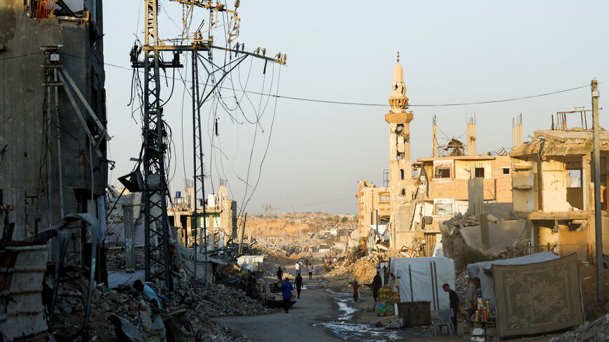 People walk past damaged electricity poles in Nuseirat, central Gaza Strip, October 31, 2025. REUTERS/Mahmoud Issa