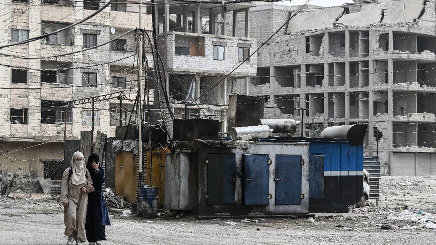 Syrian women walk past a privately owned electricity generator in the Ain Tarma area, on the eastern outskirts of the capital Damascus