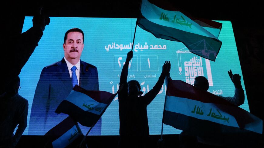 Supporters of incumbent Iraqi Prime Minister Mohammed Shia al-Sudani wave national flags in front of a screen displaying his portrait as they celebrate following the announcement of preliminary election results in Baghdad on Nov. 12, 2025.