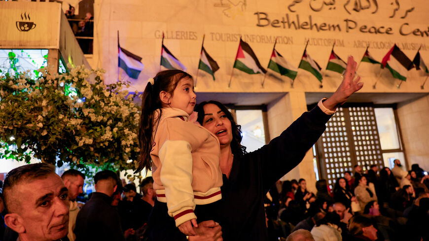 A woman holding a child gestures as Palestinians light up a Christmas tree in Manger Square outside the Church of the Nativity, in Bethlehem, in the Israeli-occupied West Bank, December 6, 2025. REUTERS/Mussa Qawasma